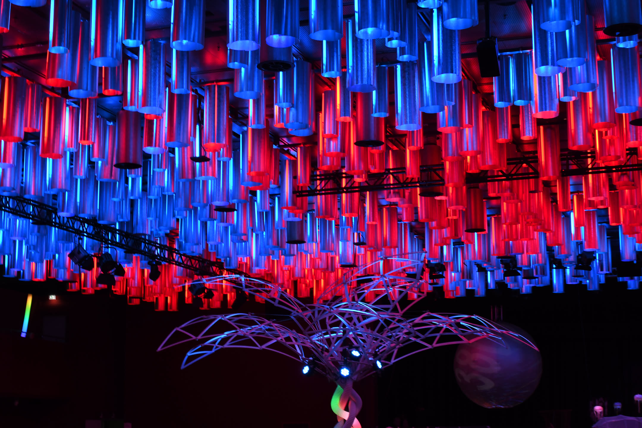 Multi-coloured lanterns hanging down from the ceiling, above a wireframe metal sculpture in the shape of a tree.